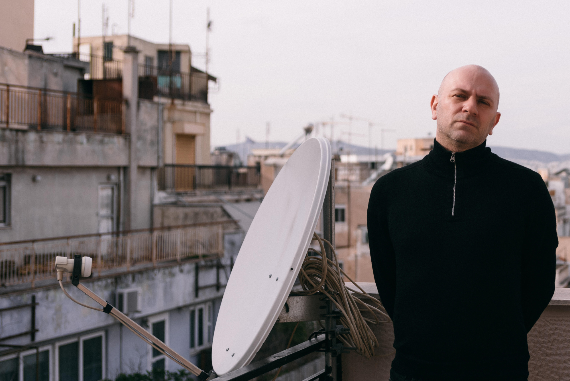 portrait of Voltnoi Brege, co-director of stegi.radio. Photographed on a balcony, next to a satellite dish, with other houses in the background